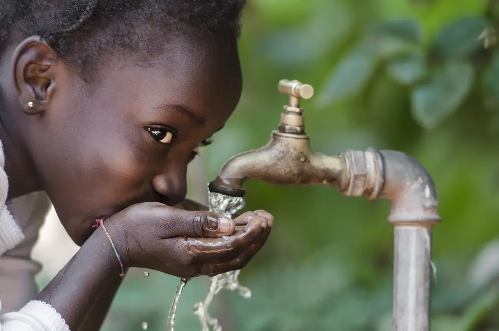 A young African girl drinking water from a communal tap